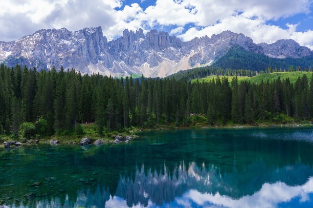 Photo of mountains, trees, a body of water, and clouds.