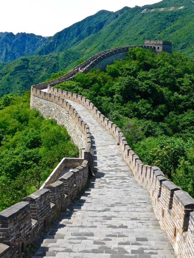 The Great Wall of China as seen from above surrounded by lush foliage and trees.