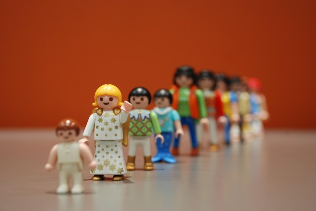 a photo of little people dolls lined up, wearing colorful little outfits, with plastic hair, on a white surface with a red background, very colorful, reminiscent of fisher price people