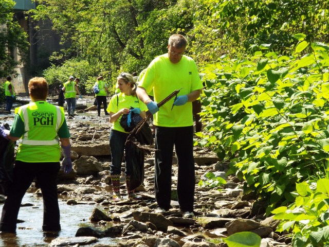 Photo of people wearing neon green vests as they are outdoors doing yard work.