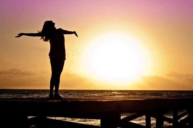Image of a woman standing arms uplifted enjoying the sunshine